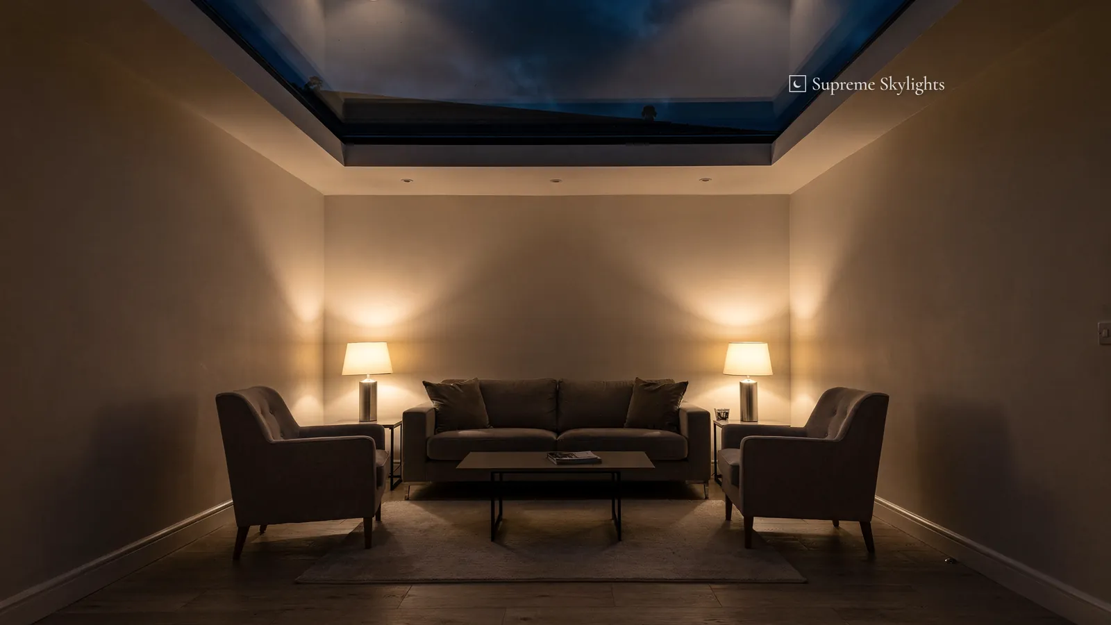 An extension sitting room after dark, two table lamps lit beside the sofa and the rooflight glass black